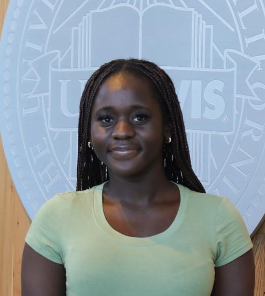 Young woman with braided hair smiling in light green shirt, pale blue university seal background