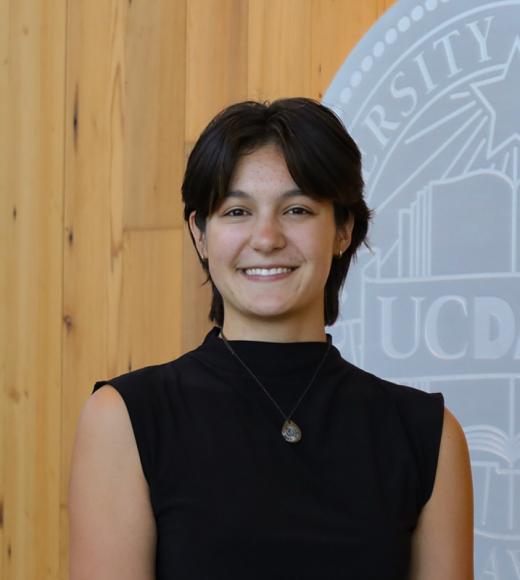 Portrait of smiling young woman in black sleeveless top against wood and gray university backdrop