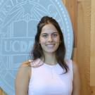 Smiling young woman in white sleeveless top standing before a university seal