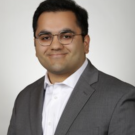 Formal headshot, man in gray suit and glasses, neutral light-gray background