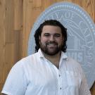 Smiling man in white shirt before wooden wall with large circular municipal seal logo