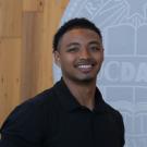 Smiling young man in black polo before wooden wall and partial circular emblem