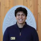 Young smiling man in navy sweater with name badge before university seal